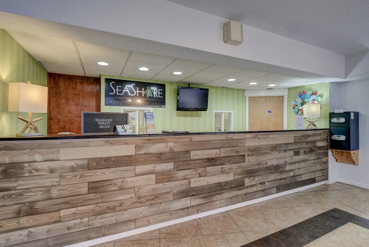 A cozy reception area with a prominent SEASHORE sign, glowing lighting fixtures, decorative wall art, and a tidy reception desk. The space feels both friendly and inviting, suggesting a boutique coastal experience.
