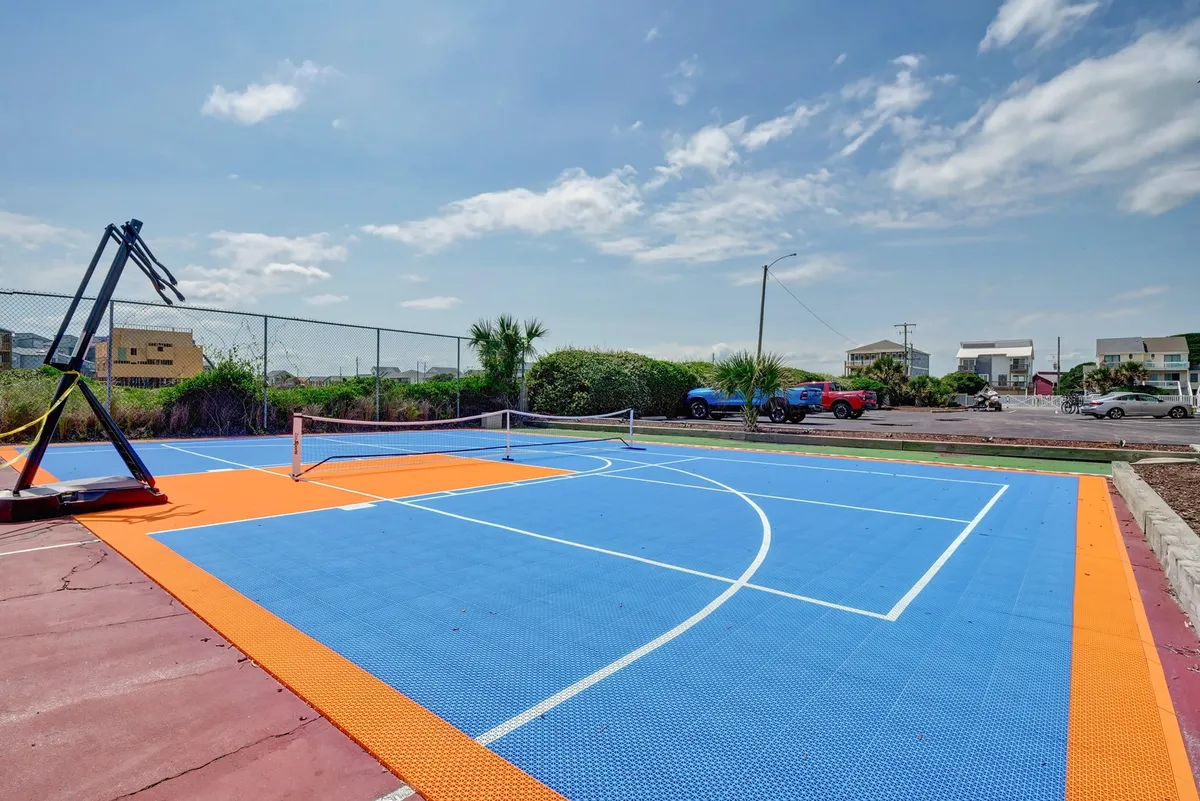 A vibrant, outdoor multi-sport court featuring a basketball hoop and tennis net, set against a colorful court surface. The area is spacious, inviting groups to engage in friendly competitions under open skies, surrounded by the refreshing atmosphere of the outdoors.