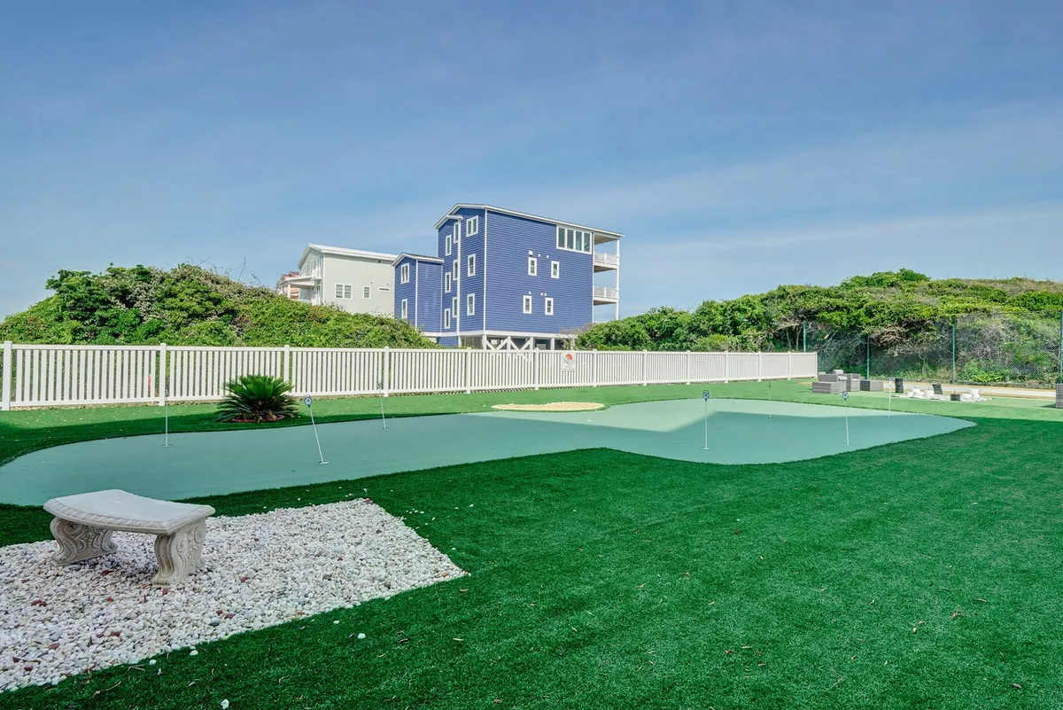 An artificial putting green framed by decorative stone benches and lush greenery, offering a relaxed yet social setting for groups to enjoy a casual golf practice or unwind together outdoors.