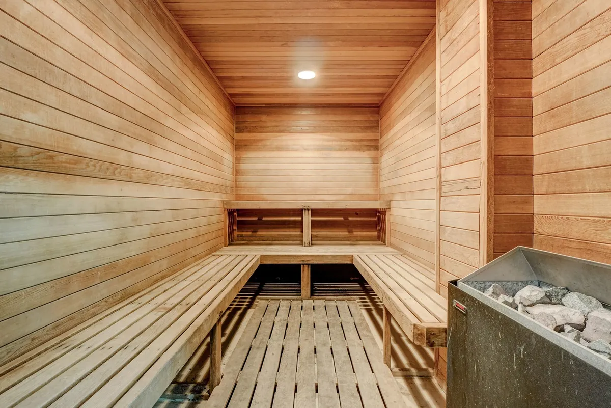 A serene sauna room lined with natural wood, featuring a stone heater and wooden benches. The space is intimate and tranquil, ideal for relaxation and rejuvenation after a workout or busy day.
