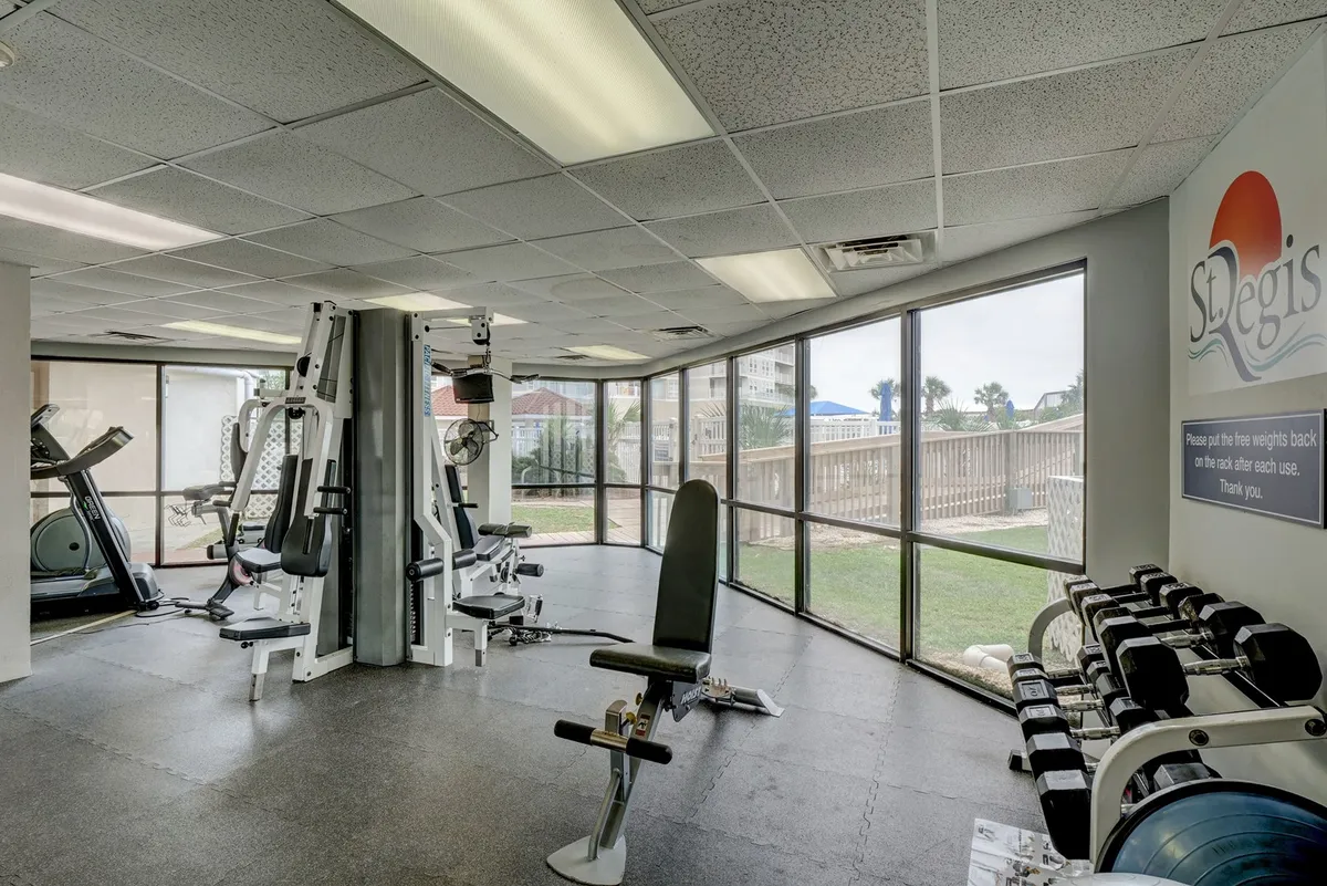 A bright, modern fitness center filled with exercise equipment, including a fitness bench and other workout machines. Large windows provide plenty of natural light and offer glimpses of the outdoor surroundings, creating an energetic atmosphere for both solo workouts and group classes.