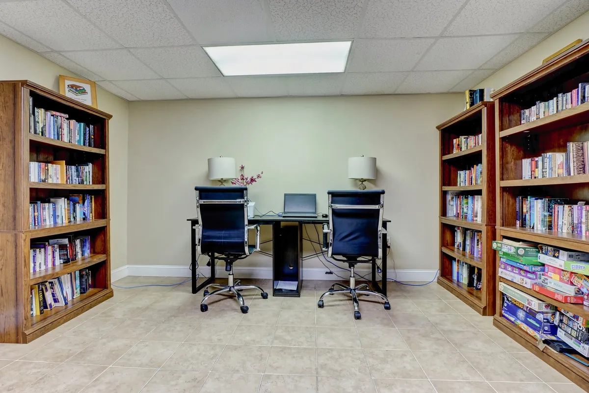 A serene reading and workspace area with built-in bookshelves, comfortable chairs, and desks—bathed in natural light from large windows. The environment is both functional and welcoming, allowing for both social interaction and private moments.