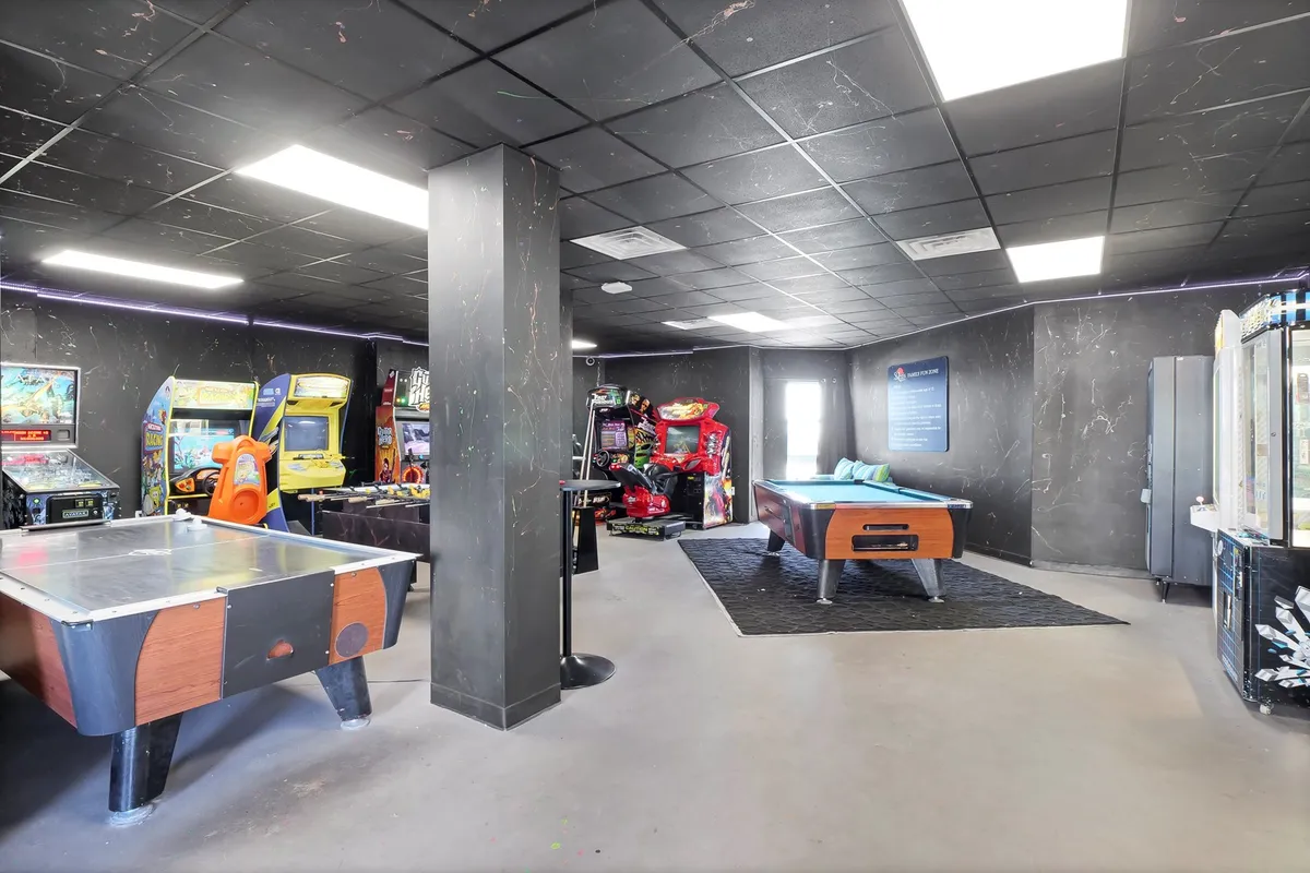 A lively interior recreation room featuring arcade machines, a pool table, and an air hockey table. The space is arranged for group games and casual family entertainment.