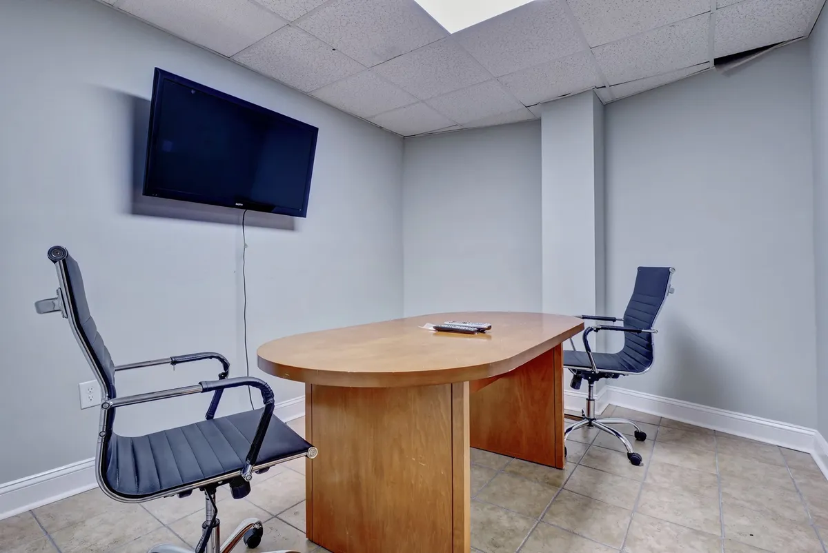 A sleek business center setup with a wooden conference table, ergonomic chairs, and a wall-mounted TV for presentations or virtual meetings. The space feels focused and professional, perfect for productivity within the resort environment.